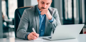 Cuidados ao vender um precatório - Pessoa analisando e anotando ao lado de seu notebook.